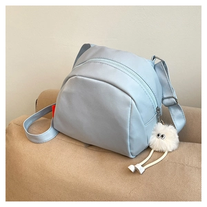 Detail of light blue nylon crossbody bag with zipper closure and white plush eye pendant