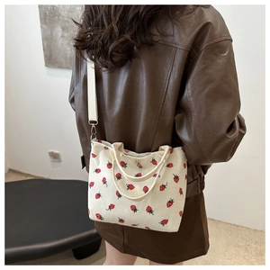 Detail of strawberry corduroy tote bag showing the adjustable strap on a model shoulder