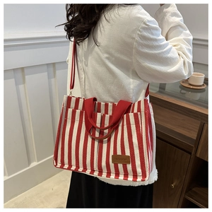 Detail of red and white striped canvas tote bag showing the brown leather logo and handle