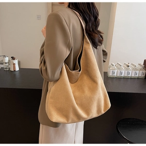 Detail view of large camel suede tote bag with minimalist hobo design on model shoulder