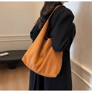 Detail view of large orange suede tote bag worn over a black winter coat for autumn fashion
