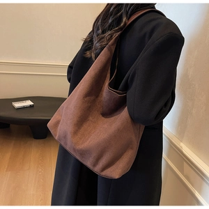Side view of a dark brown suede tote bag worn by a model in a minimalist setting
