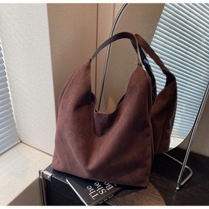 Detail of a large dark brown suede hobo tote bag on a black table with artistic lighting
