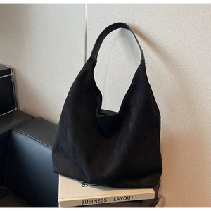 Close-up of minimalist black hobo bag in suede texture placed on white decorative books