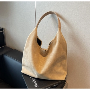 Detail of khaki suede tote bag with leather strap placed on a leather sofa for daily commute