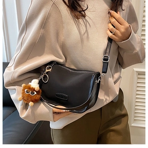 Close-up of black crossbody bag with fashion emblem and brown plush bear charm accessory