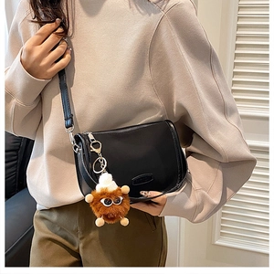 Detail of black crossbody bag with FASHION logo and a brown plush monster charm