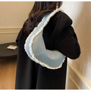 Detail shot of a light blue denim crescent underarm bag with white fringe trim