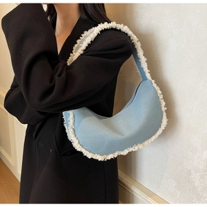 Détail du sac hobo bleu clair avec bordure à franges blanches porté à l'épaule