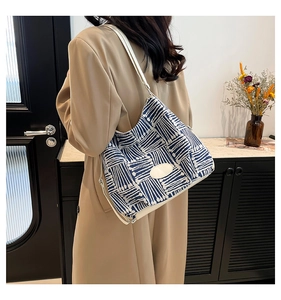 Detail of blue and white geometric canvas tote bag with white leather strap shown on shoulder