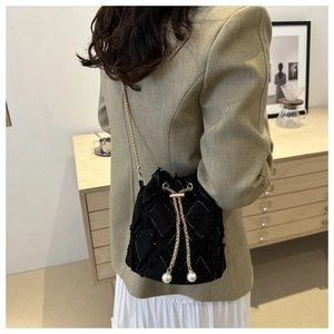 Détail du sac seau en denim noir avec texture matelassée, chaîne dorée et perles
