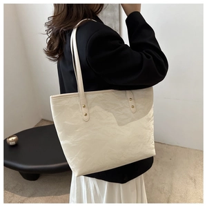 Model wearing a cream white tote bag with a crinkled texture and minimalist metal rivets