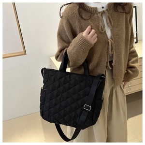 Detail of black quilted tote bag showing large diamond stitching and side pocket