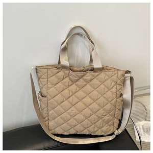 Detailed close-up of a quilted beige tote bag featuring a side pocket and adjustable strap