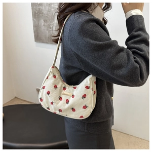 Detail of cream corduroy shoulder bag featuring red strawberry embroidery and gold metal hardware