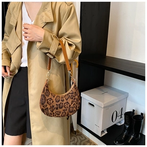 Close-up of leopard print crescent bag with brown shoulder strap worn with a beige trench coat