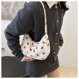 Detail of white corduroy crescent bag featuring red strawberry print and silver plaque