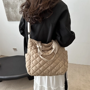 Khaki quilted tote bag with large diamond patterns and adjustable strap worn by a model