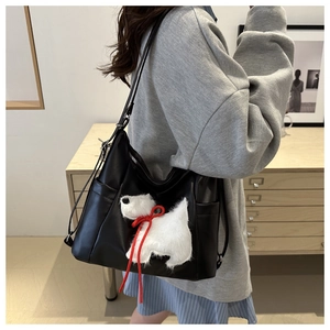 Detail of a black leather tote bag with a cute plush puppy patch and red ribbon accent