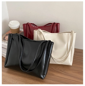 Three minimalist tote bags in black beige and burgundy displayed on a wooden desk
