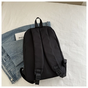 Rear view of black nylon backpack featuring padded adjustable straps and top handle on denim