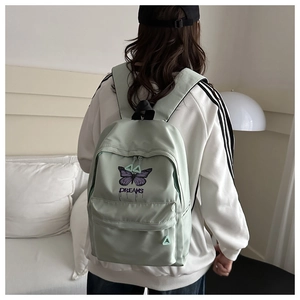 Detailed view of butterfly embroidery and DREAMS lettering on light green nylon backpack