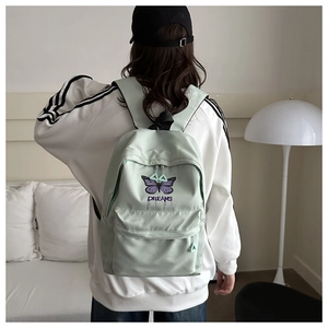 Detail view of a light green backpack with purple butterfly embroidery and dreams text
