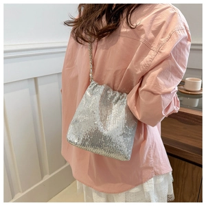Silver sequin drawstring bucket bag with gold chain strap shown on person