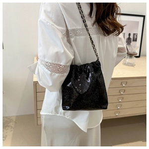 Detail of black sequin bucket bag with gold chain strap shown on person in a home setting