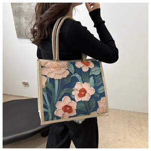 Detail of artistic floral printed tote bag with textured woven straps on female model