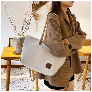 Dettaglio della borsa tote in tela con tracolla in pelle e applicazione logo premium