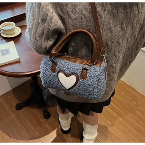 Blue sherpa cylinder crossbody bag with brown leather handles and heart patch on a table