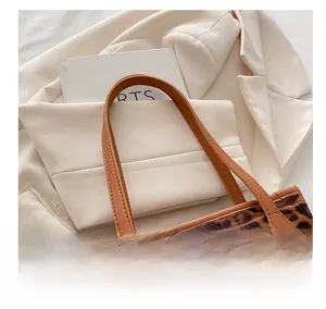 Detail of leopard print tote bag featuring brown leather handles on a white blazer