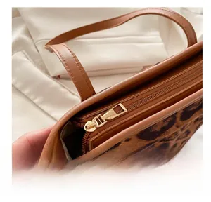 Detail of smooth gold zipper on leopard print shoulder bag with brown leather trim