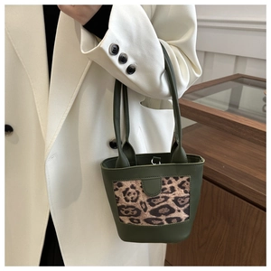 Detail of dark green bucket bag with leopard print panel held by model in white suit