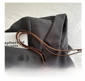 Detail of a brown leather tote bag paired with a dark grey blazer and a textured background