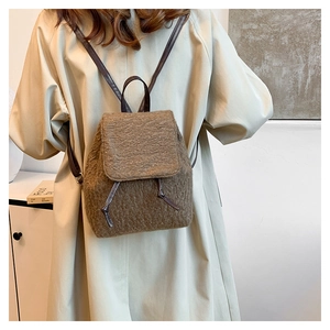 Gros plan du sac à dos en laine marron avec lanières en cuir sur manteau beige