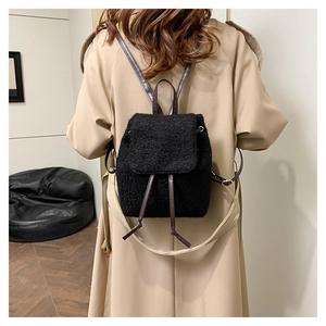 Détail du mini sac à dos en polaire noire avec sangles en cuir brun sur un trench-coat