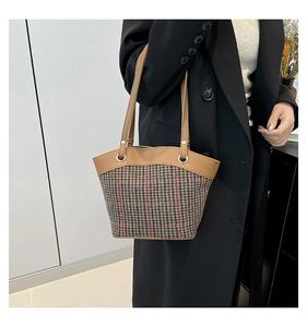 Détail du sac cabas en pied-de-poule avec anses en cuir marron sur un manteau en laine noir
