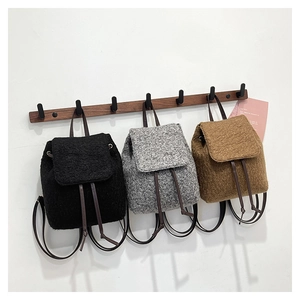 Three fuzzy faux shearling mini backpacks in black, grey, and brown hanging on wooden hooks