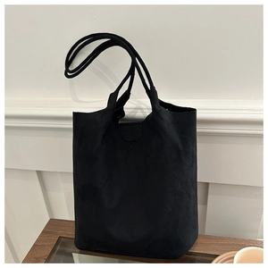 Détail d'un sac cabas noir en suédine avec de longues anses sur une table en bois