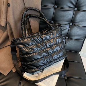 Schwarze gesteppte Daunentasche aus glänzendem Nylon mit breitem Schultergurt auf Stuhl