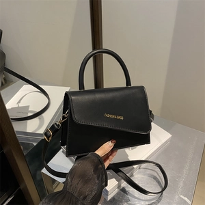 Minimalist black trapezoid leather handbag with top handle and asymmetric flap design