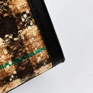 Macro detail of brown plaid tweed fabric and black leather trim on a crossbody bag