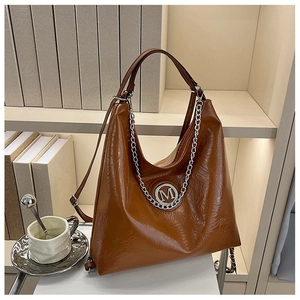 Detail van een bruine leren Hobo-tas met zilveren M-logo en metalen kettingdecoratie