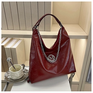 Detail van de wijnrode hobo-tas met glanzend leer en zilveren M-logo aan de ketting