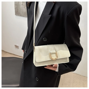 Detail einer cremefarbenen Umhängetasche mit goldener D-Schnalle am schwarzen Blazer