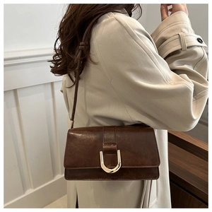 Détail d'un sac bandoulière en cuir marron foncé avec fermoir doré en U sur manteau beige