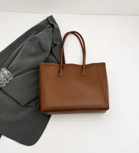 Vista dall'alto di borsa tote marrone scuro su superficie bianca con giacca grigia e decoro