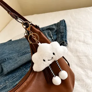 Close-up of a plush white cloud charm with a smiley face on a brown leather bag